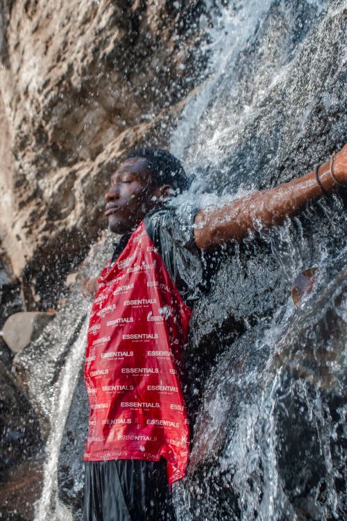 Free Adult male enjoying the refreshing splash of a waterfall in a natural rocky setting. Stock Photo