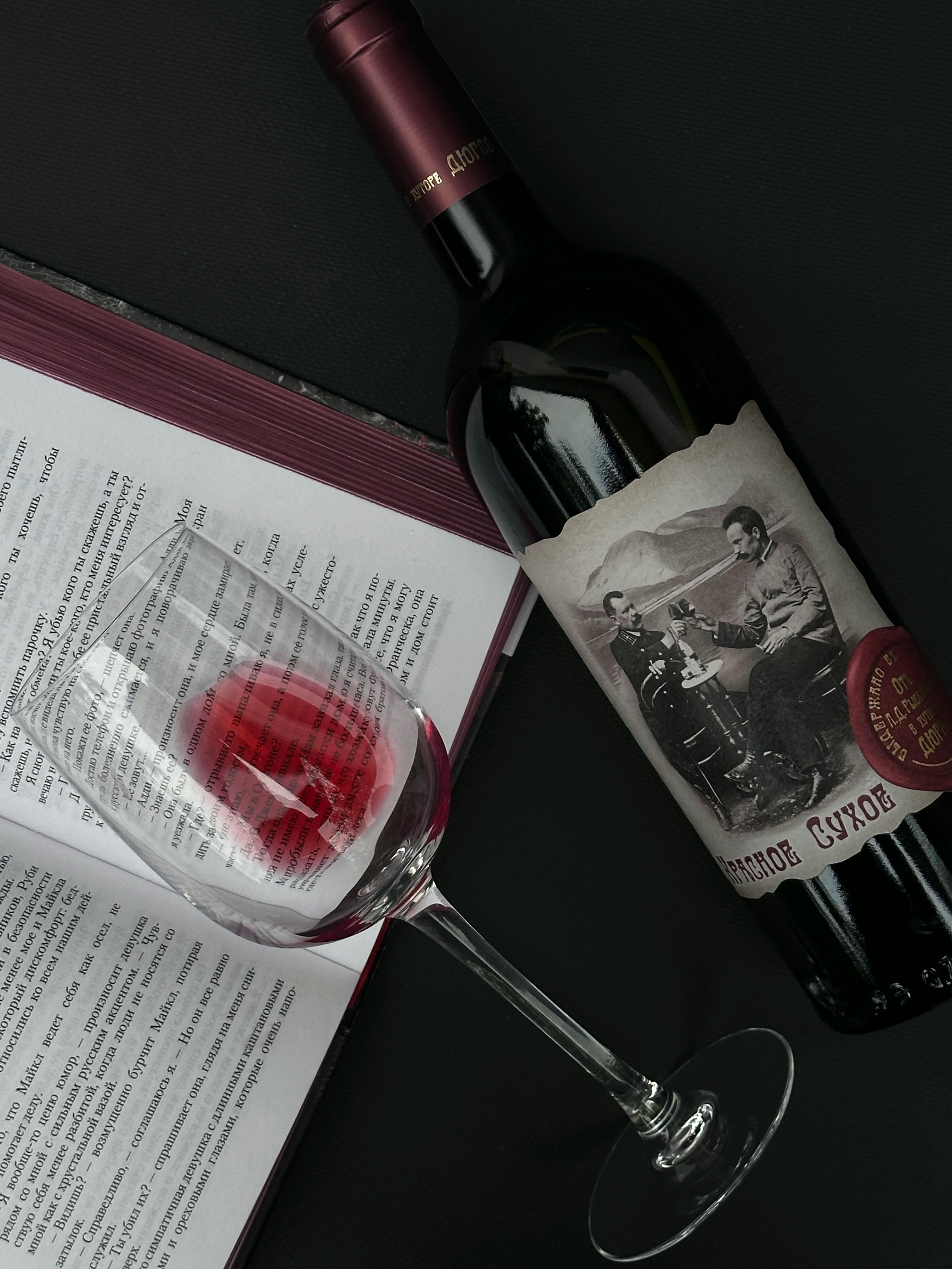 A red wine bottle with a glass and an open book on a dark background.