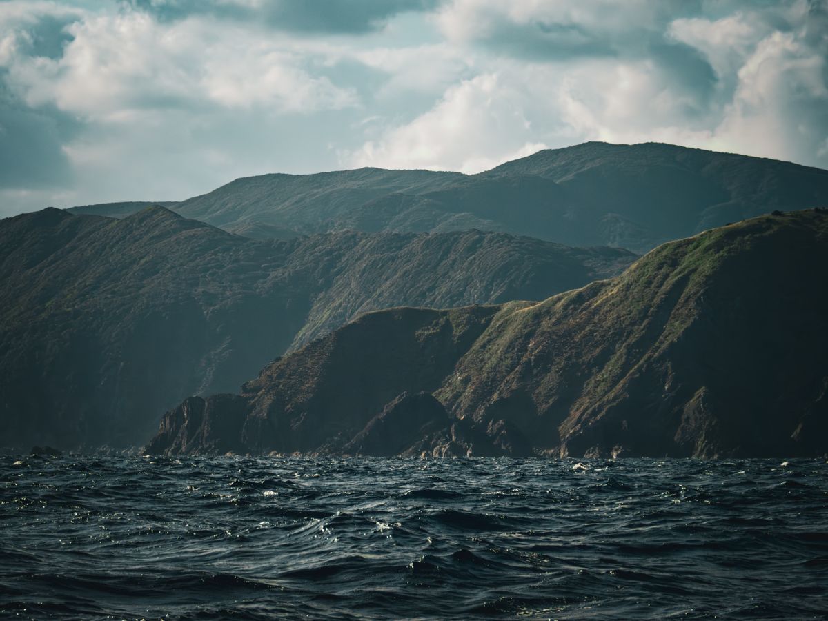 Dramatic rugged coastal cliffs rising from dark sea water under cloudy sky in Kagoshima Prefecture