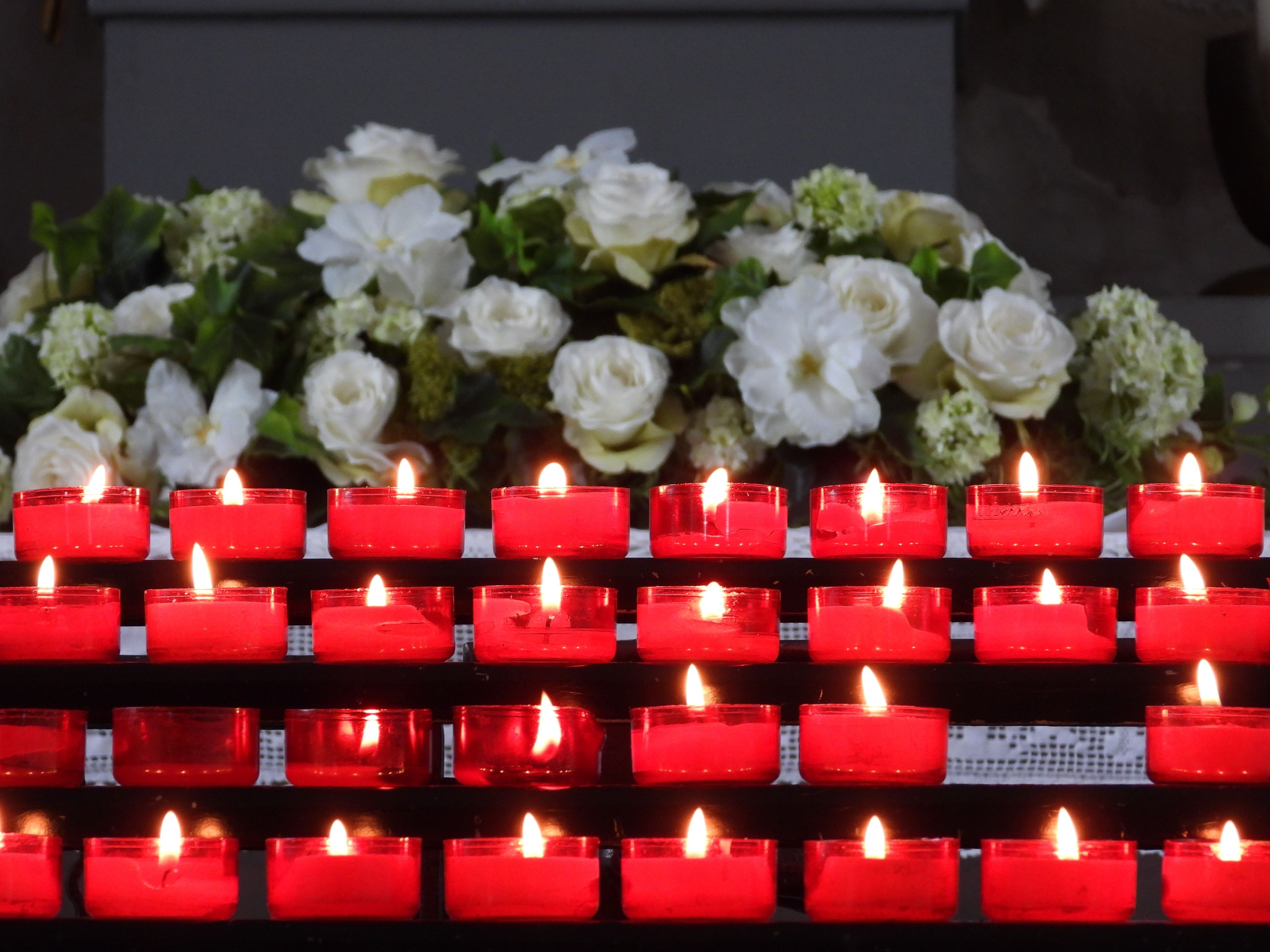 A serene arrangement of lit red candles with white flowers in the background, creating a peaceful ambiance.