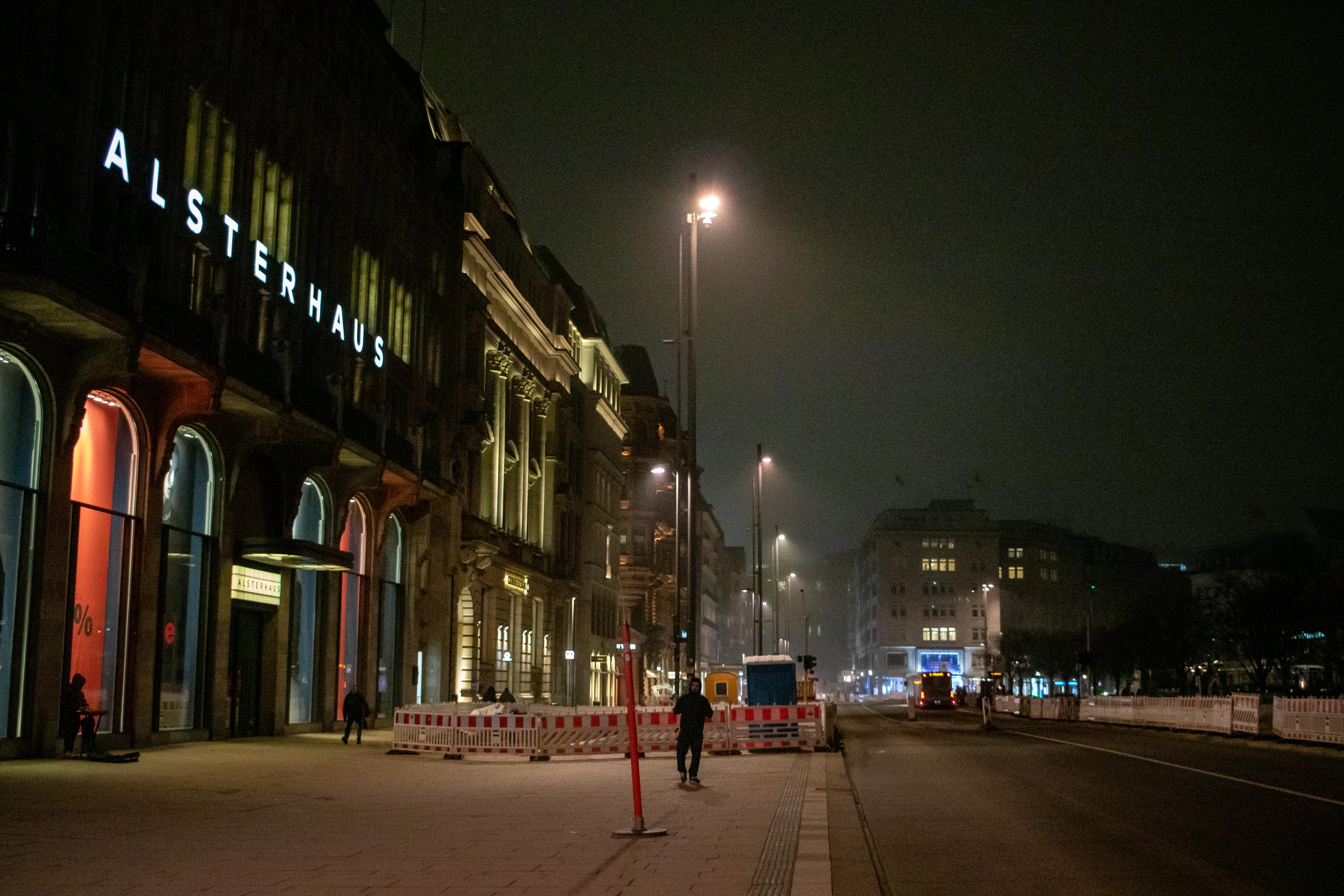 A nighttime street scene featuring Alsterhaus in Hamburg, beautifully lit under streetlights.