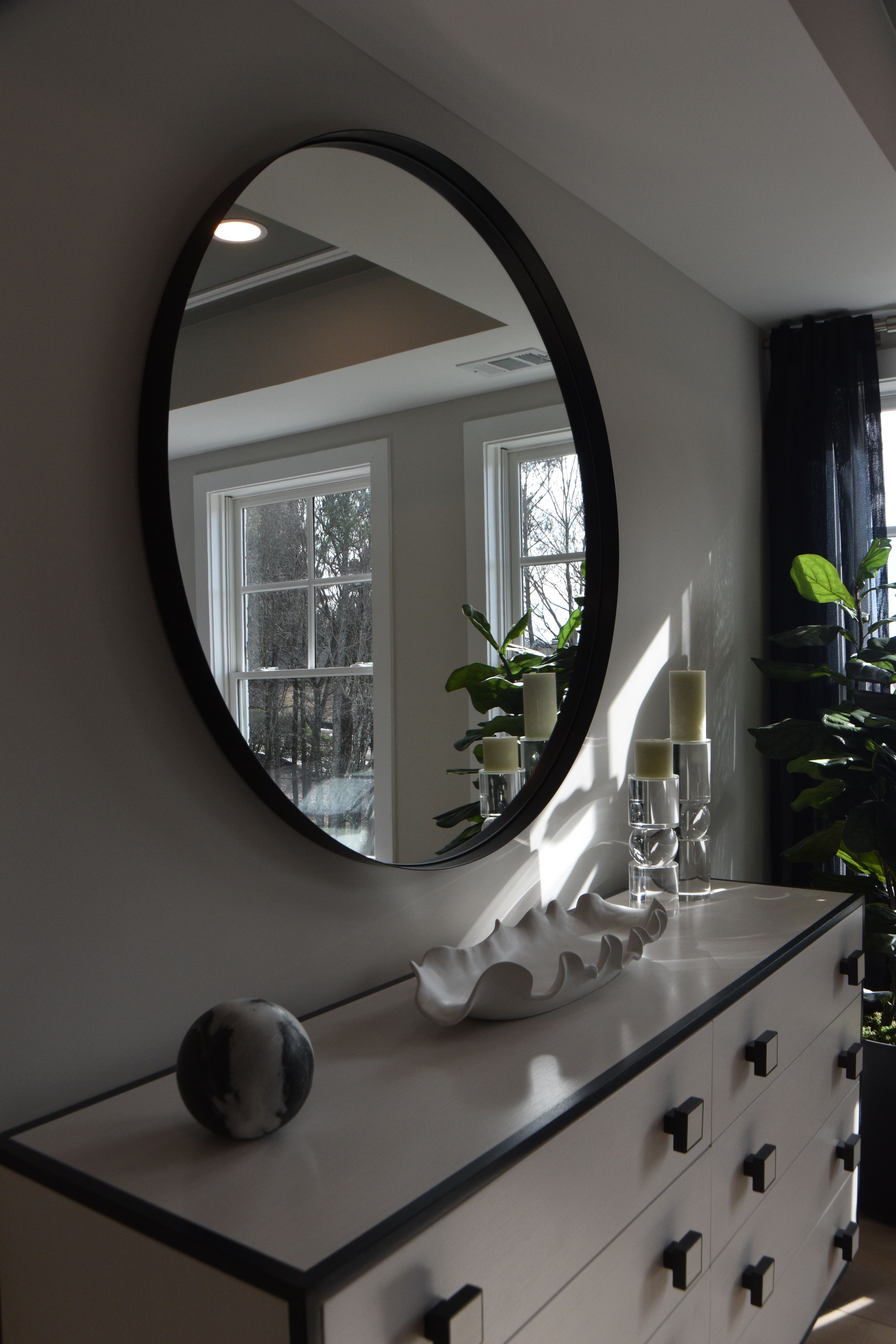 Large round black-framed mirror above a white dresser in an elegant bedroom
