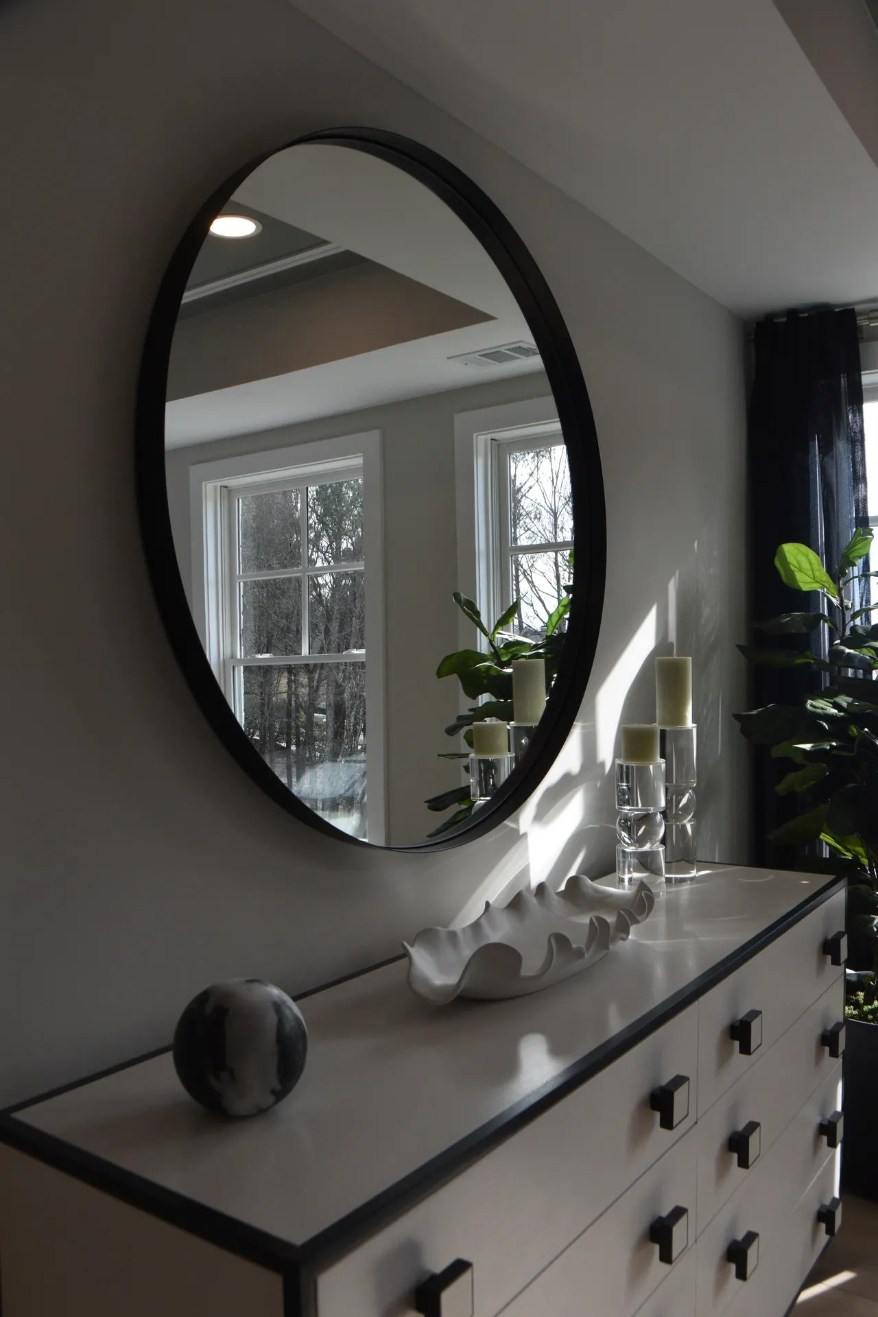 statement-round-mirror-makeup-vanity Large round black-framed mirror above a white dresser in an elegant bedroom