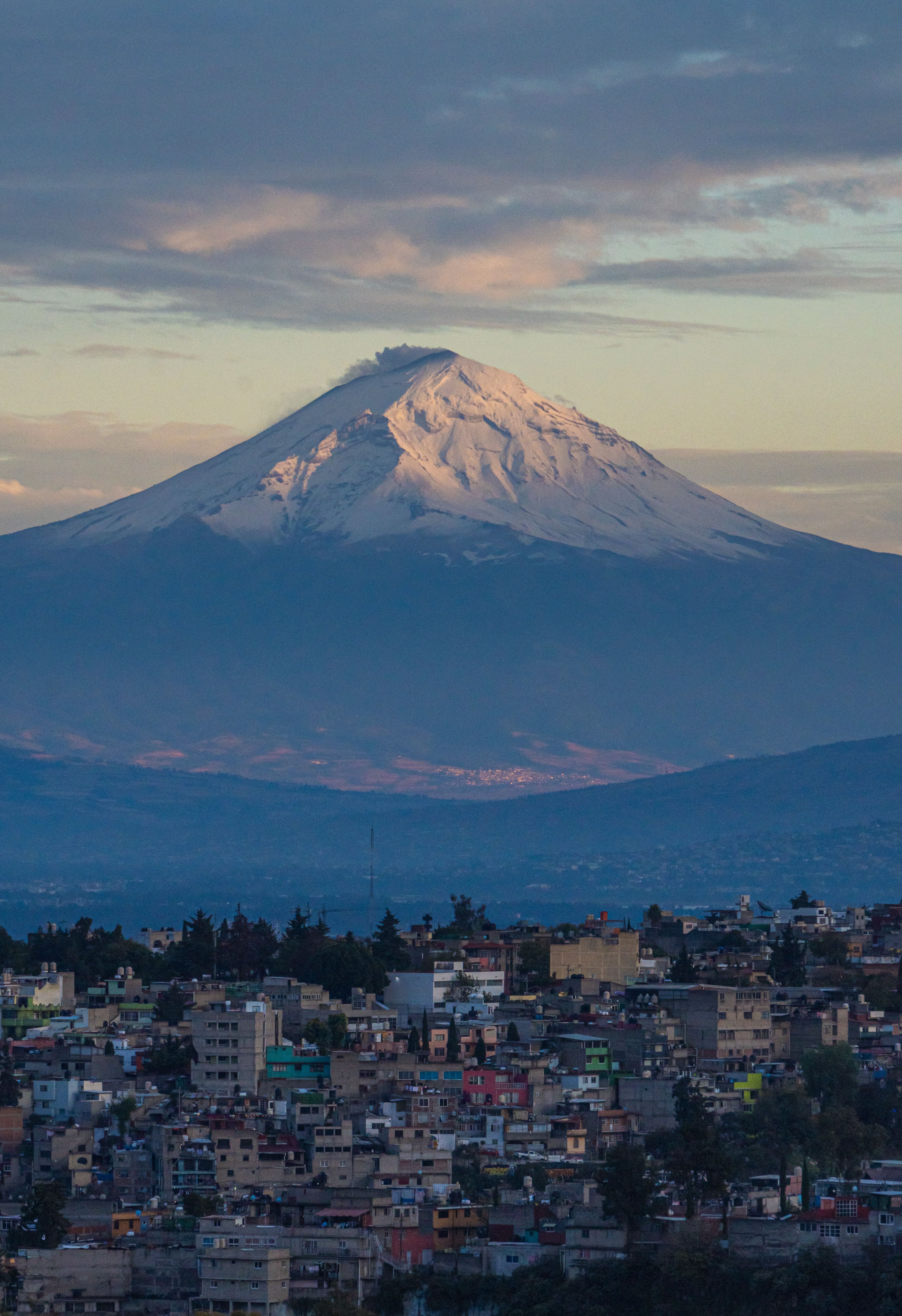 Breathtaking view of Popocatu00e9petl volcano overlooking Mexico City's urban landscape at dusk.