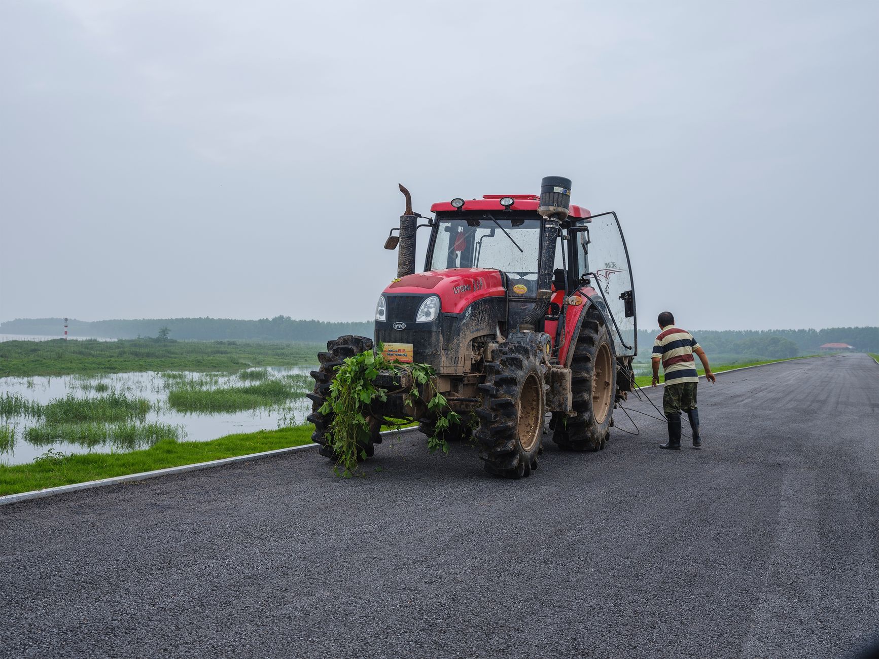 A farmer operates a red tractor on an overcast day, highlighting rural life and agriculture.