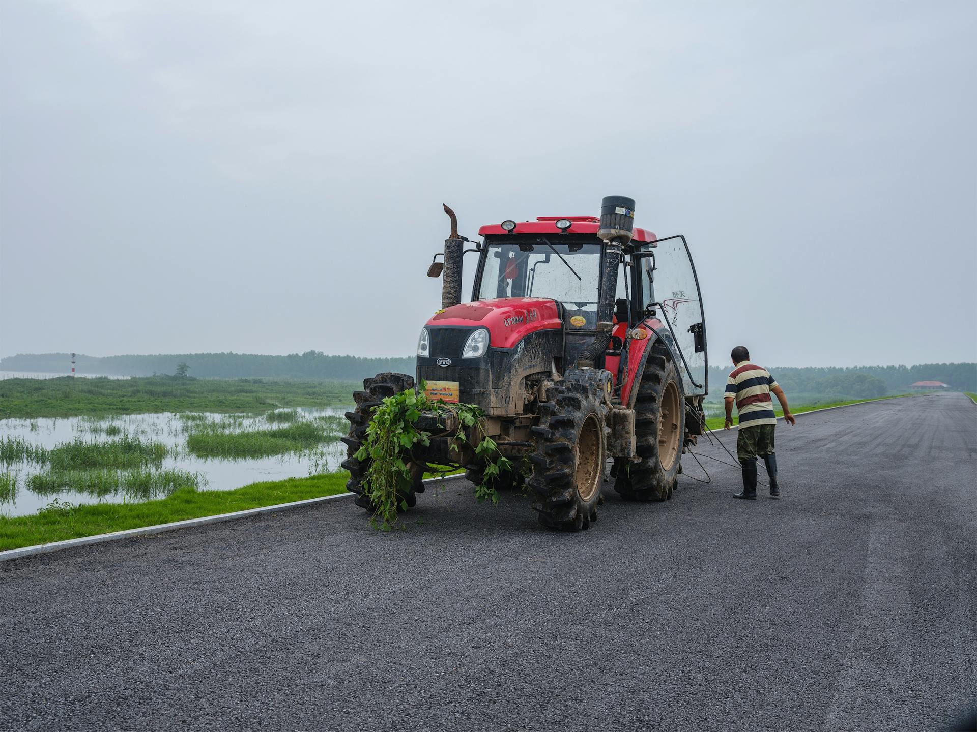 A farmer operates a red tractor on an overcast day, highlighting rural life and agriculture.