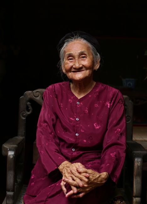 Portrait of an elderly Vietnamese woman in traditional dress, smiling warmly while seated.