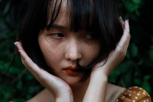 一位年轻女子双手托着脸，在自然背景下的亲密肖像