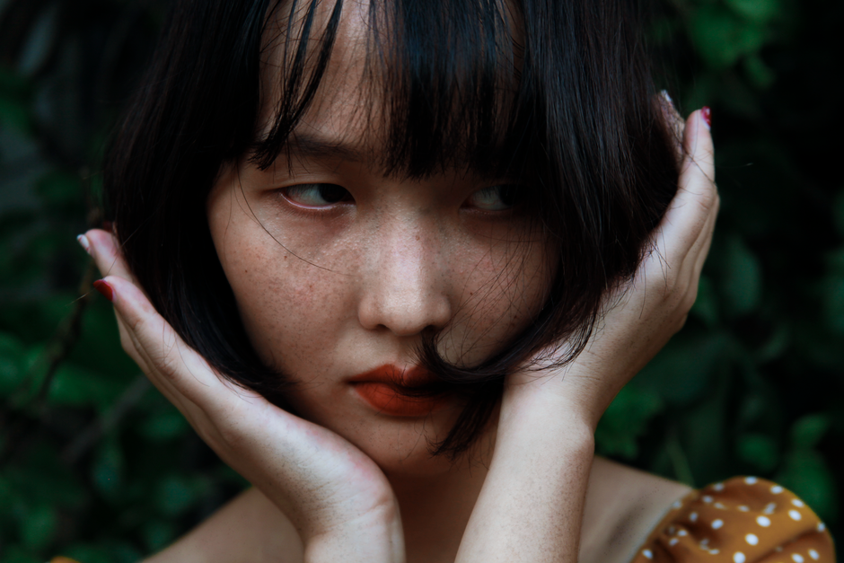 Intimate portrait of a young woman with nature background, hands on face.