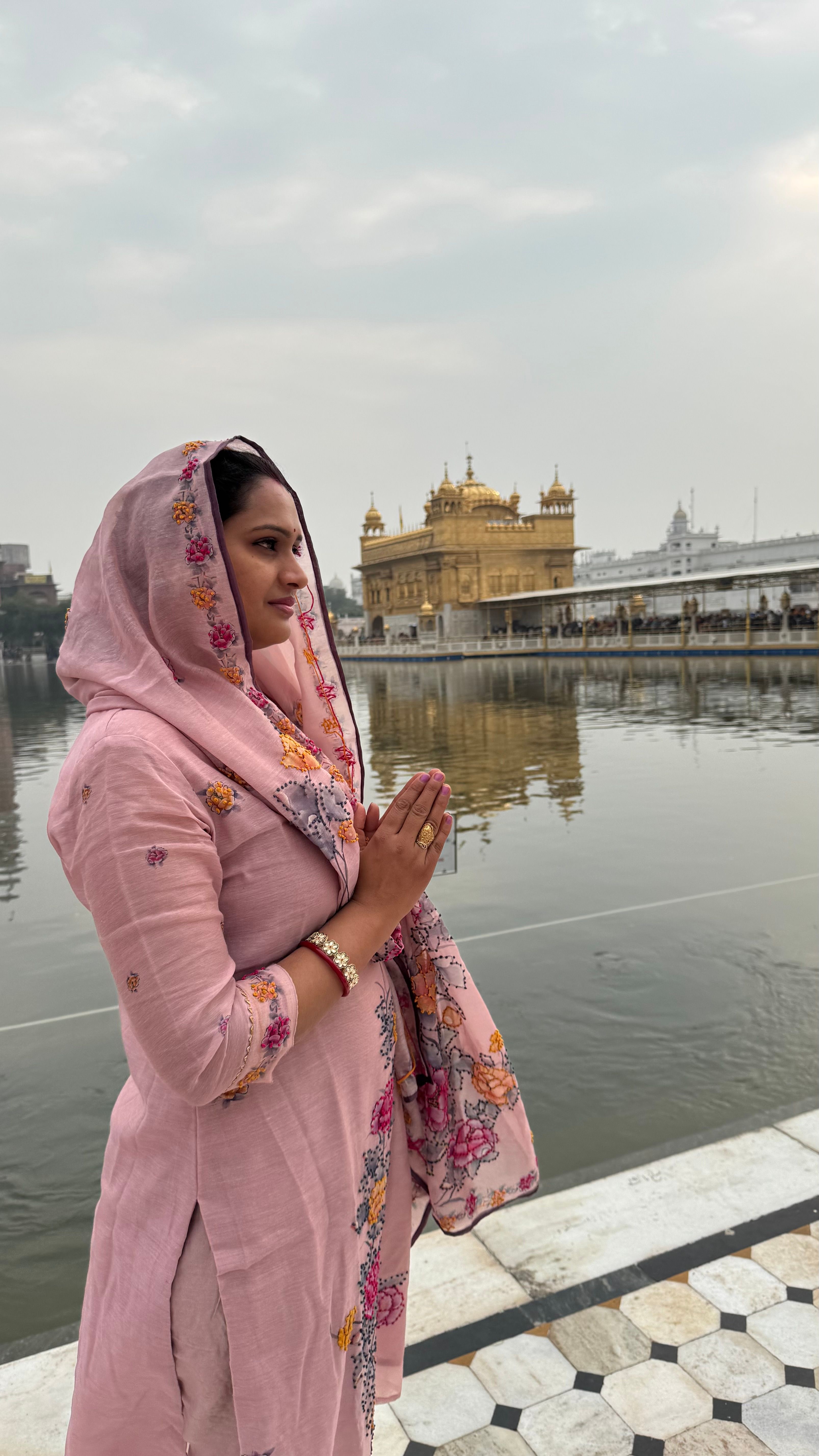 A woman in traditional attire prays near the Golden Temple, Amritsar, India, reflecting spirituality.