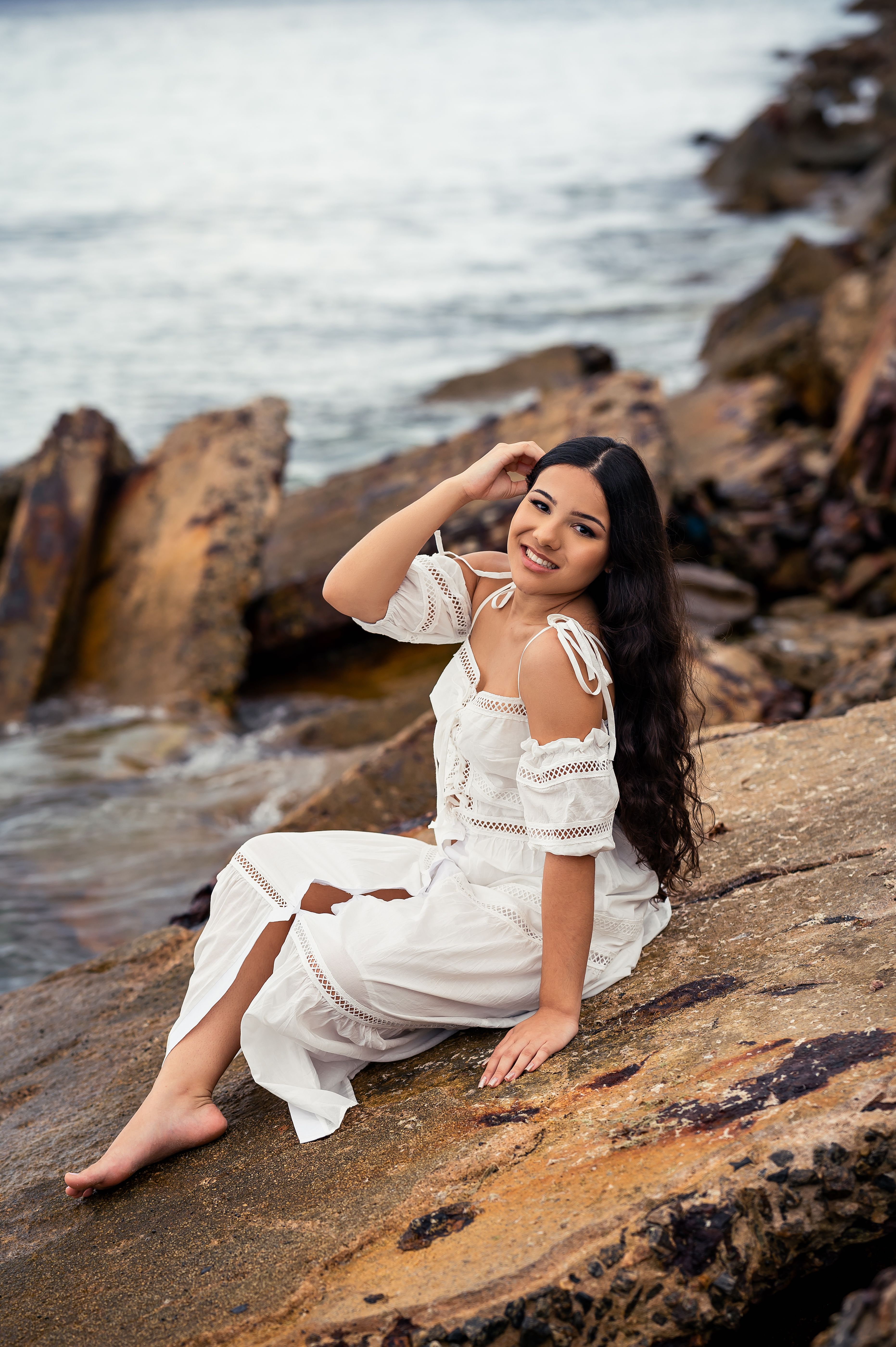 Woman sitting on rocky beach in white dress · Free Stock Photo