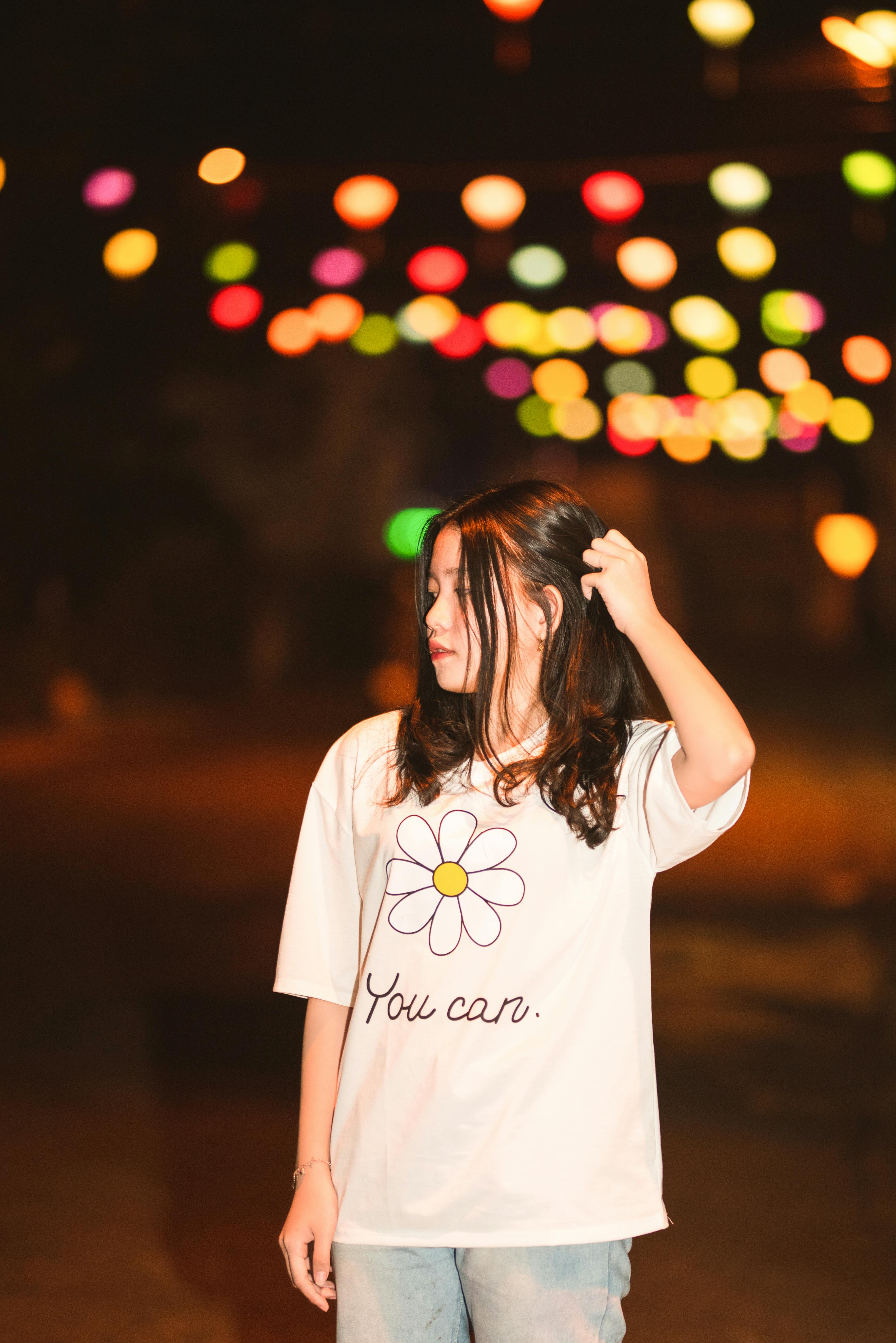 A woman standing under vibrant bokeh lights at night, embodying casual confidence.