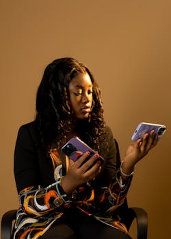 Stylish young woman in office chair comparing two smartphones in a warm-toned setting.