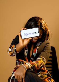 A stylish woman holding a smartphone displaying the Bennybit logo in a business setting.