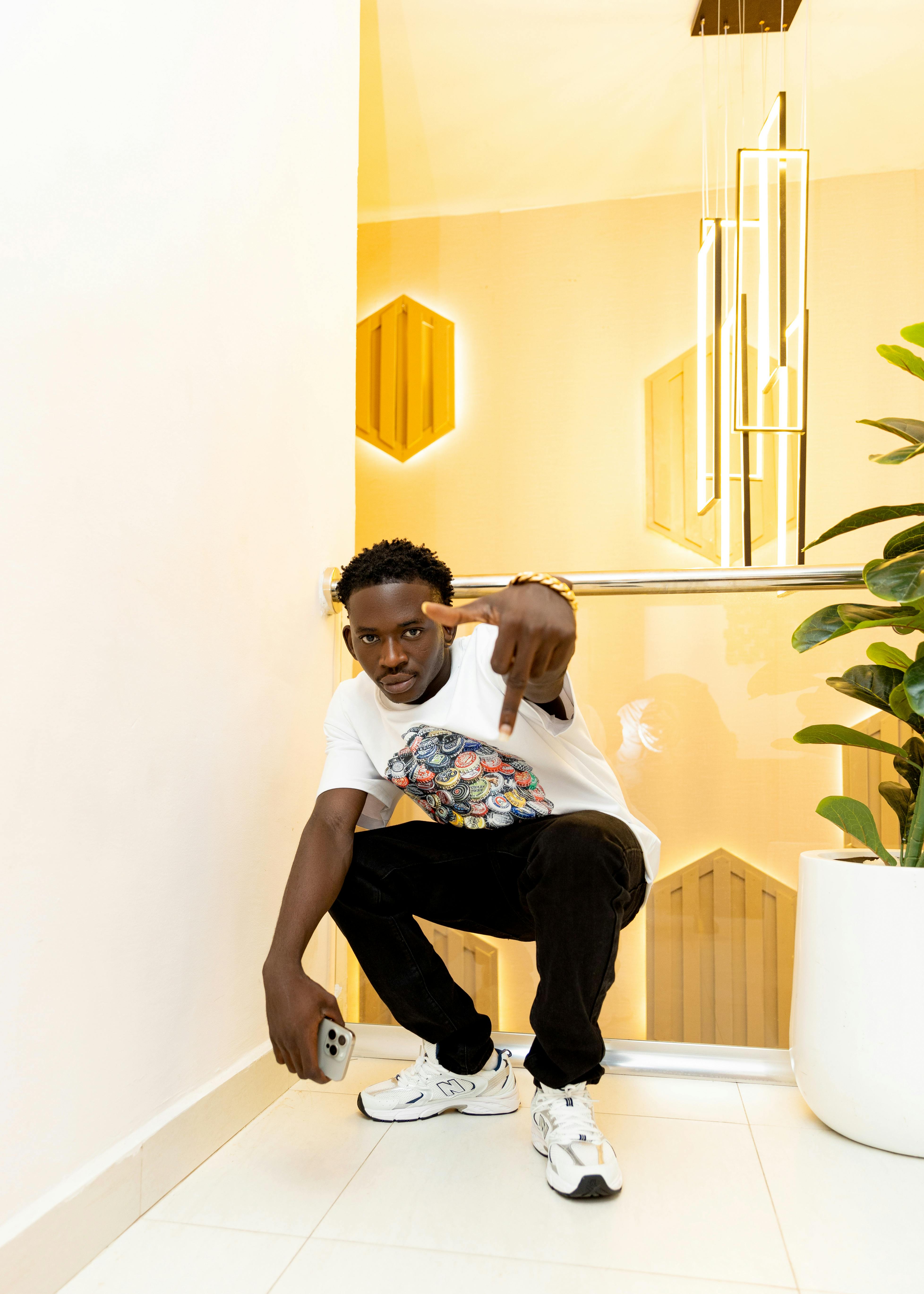 Man crouching indoors with modern decor and stylish outfit.