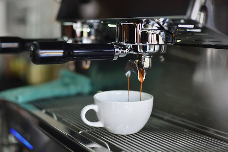 White Ceramic Mug On Espresso Machine Filling With Brown Liquid