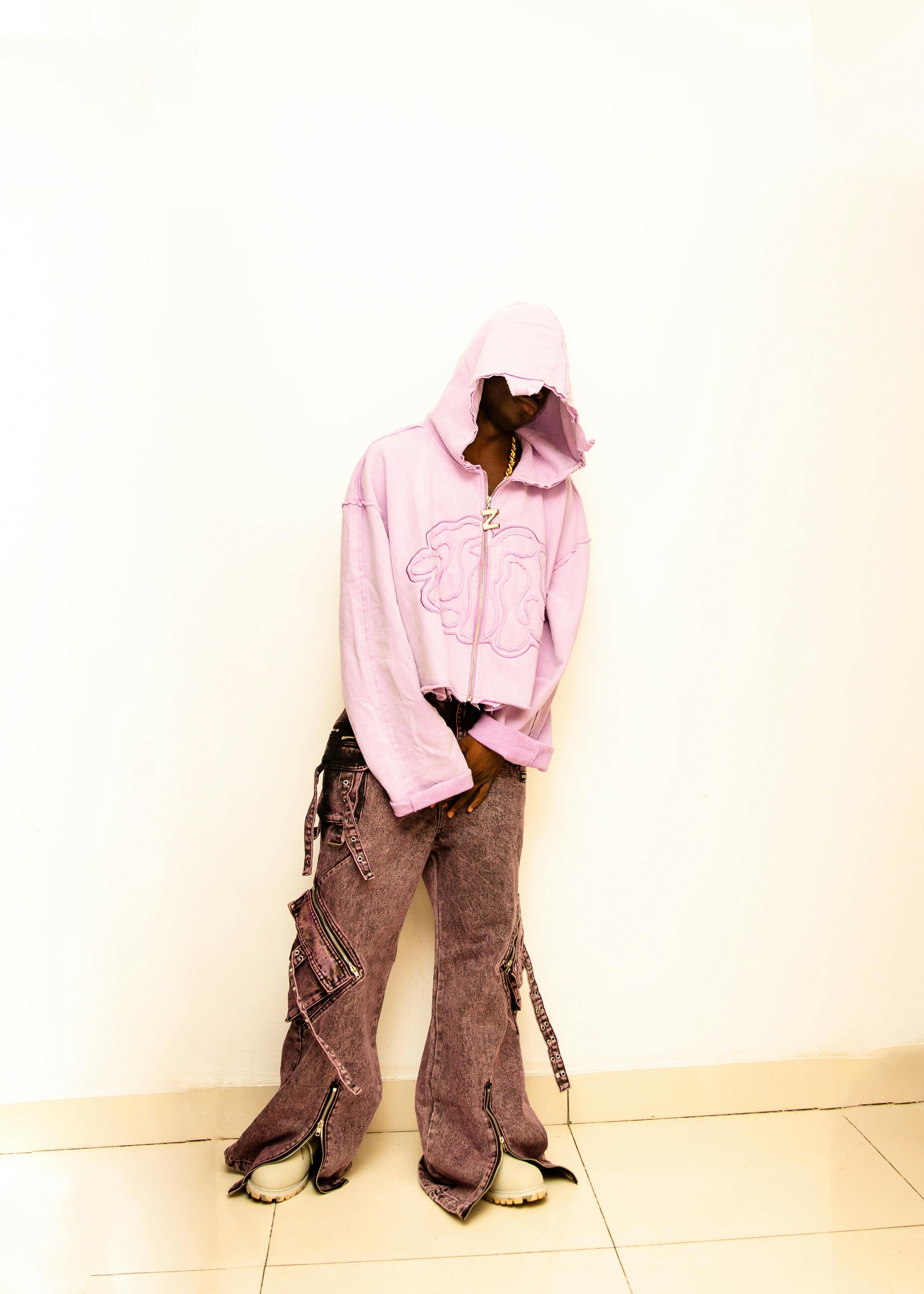бесплатная Молодой человек в стильной розовой толстовке с капюшоном и мешковатых штанах позирует в помещении. Заявление городской моды. Стоковое фото