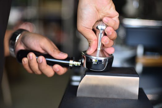 Close-up of a barista's hands using a tamper to prepare espresso in a portafilter.