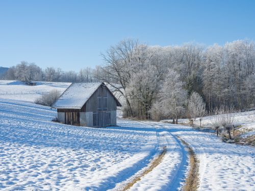 Free A picturesque snowy scene featuring a rustic barn and frosty trees under a clear blue sky. Stock Photo