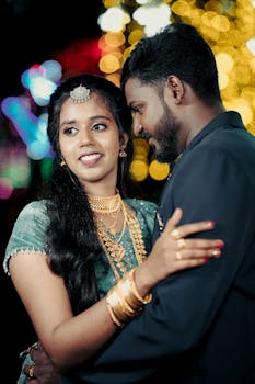 Beautiful South Asian couple embracing at a festive Indian wedding with vibrant bokeh lights.