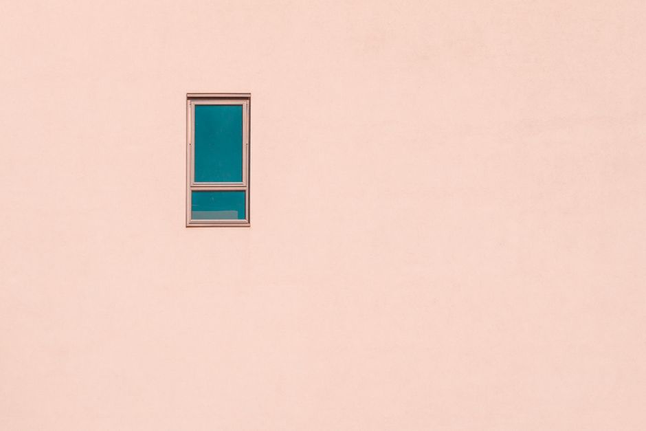 A minimalist pastel pink wall featuring a single rectangular window, offering ample negative space.