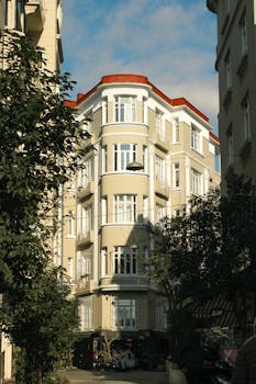 Elegant corner building with ornate architecture and red roof in sunny European city.