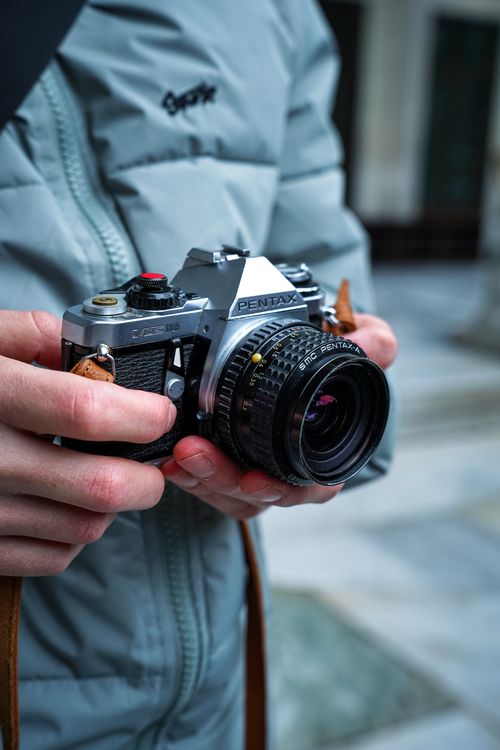 Free Close-up of hands holding a classic Pentax camera, dressed in a winter coat, symbolizing photography passion. Stock Photo