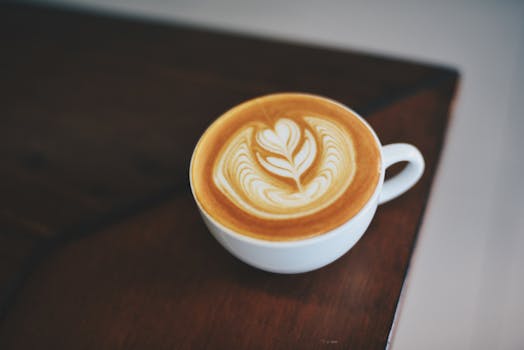 深色木桌上的白色瓷杯里，盛着一杯制作精美的拿铁咖啡，搭配着复杂的泡沫艺术