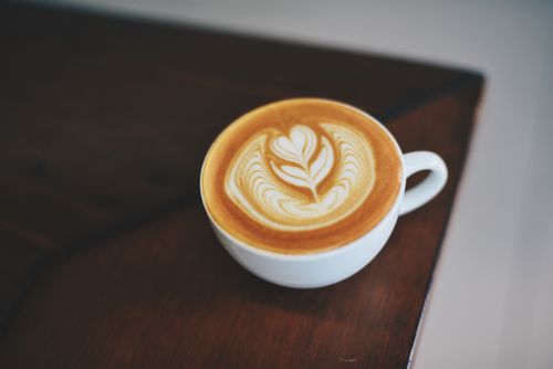 Free A beautifully crafted latte with intricate foam art in a white porcelain mug on a dark wooden table. Stock Photo