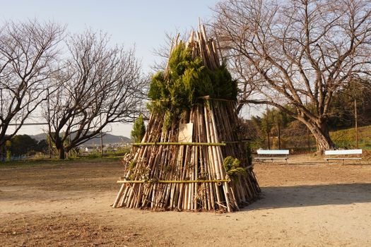 Bamboo and greenery structure in a park with benches and bare trees under a clear sky.