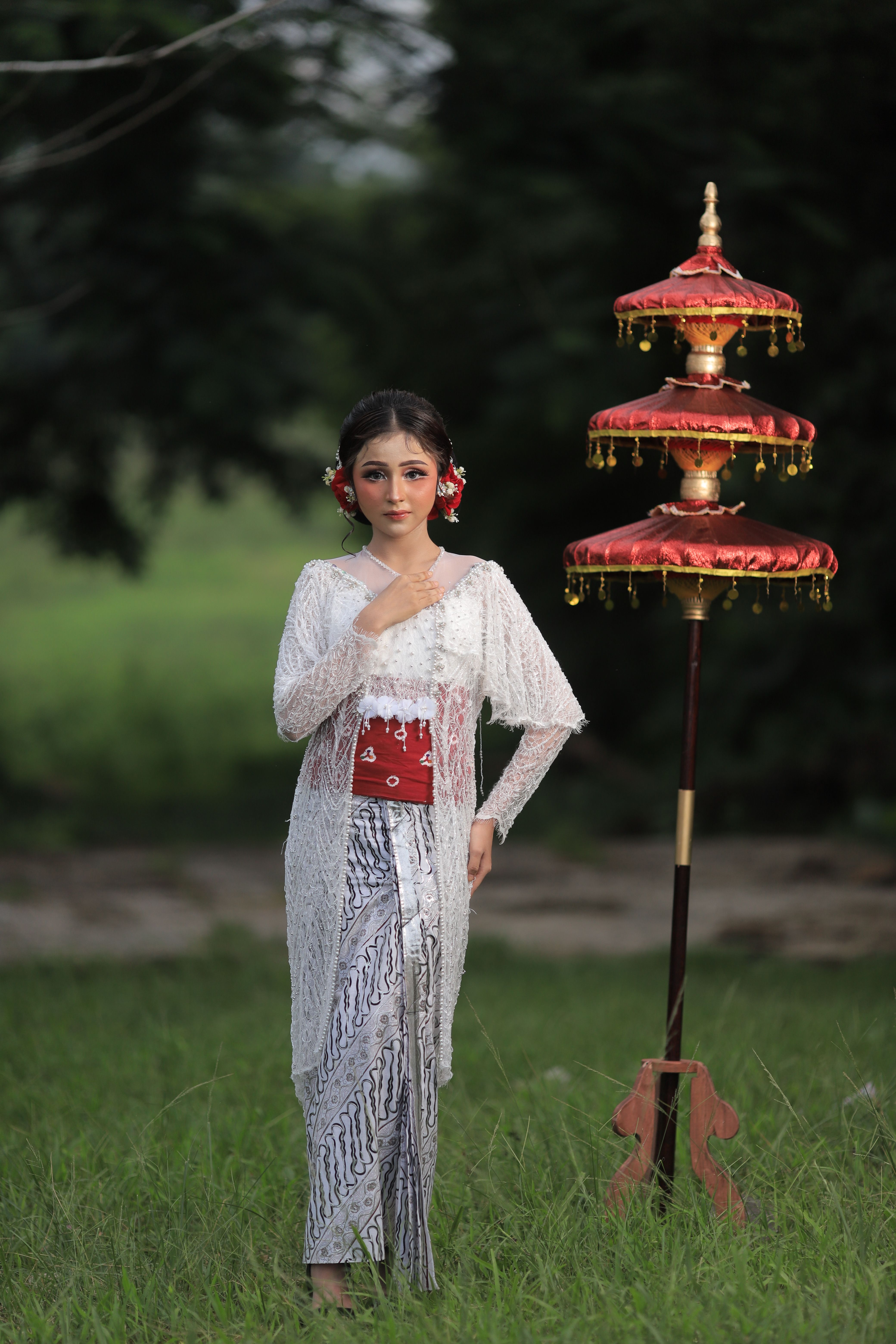 Woman in traditional Balinese dress posing outdoors beside ceremonial umbrella.