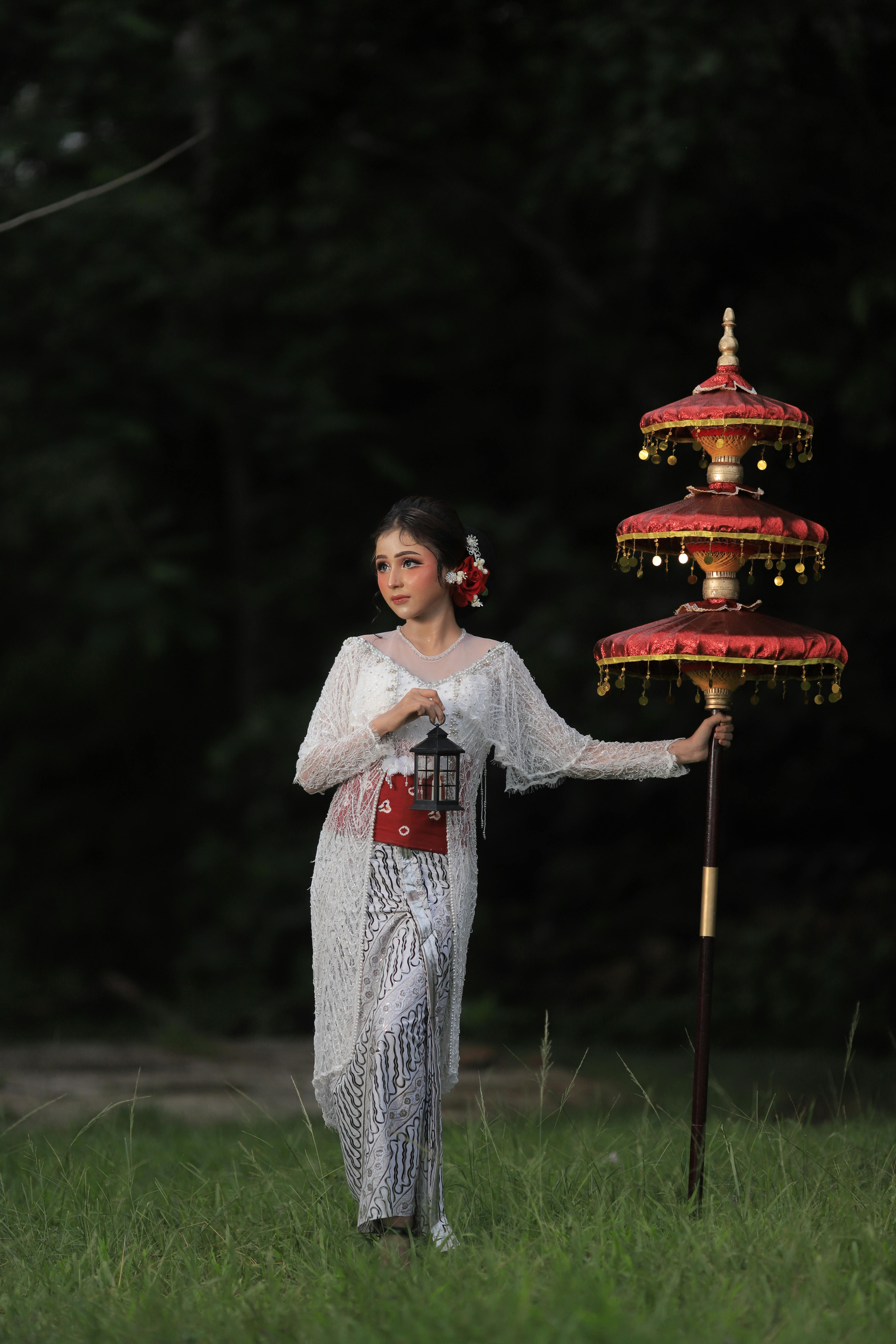 Graceful woman in traditional clothing stands with a decorative parasol outdoors.