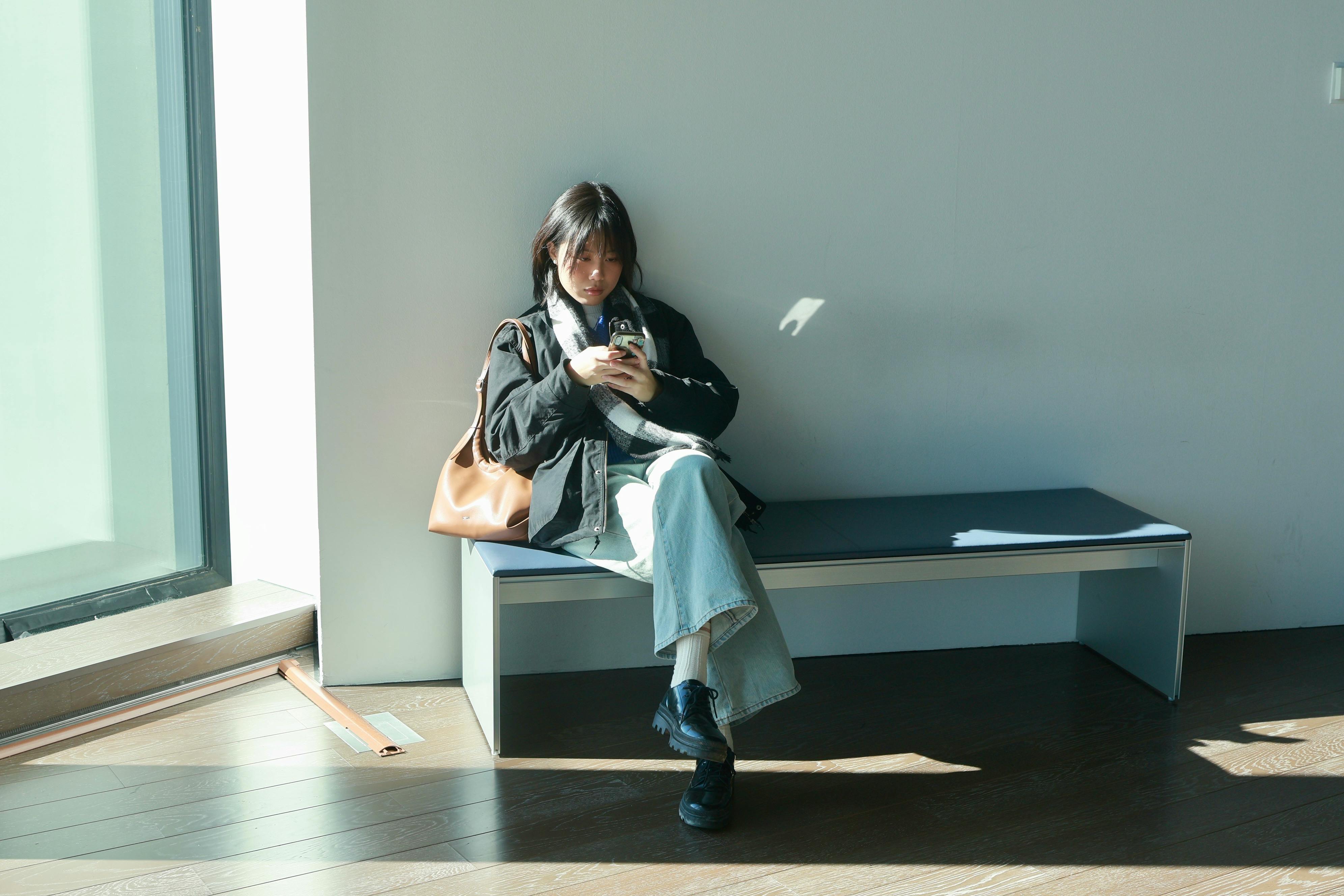 A woman relaxes on a bench indoors, using a smartphone. Location: Tokyo.