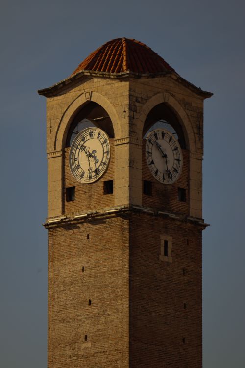 Free A historic clock tower featuring dual clock faces under dramatic sunset lighting. Stock Photo