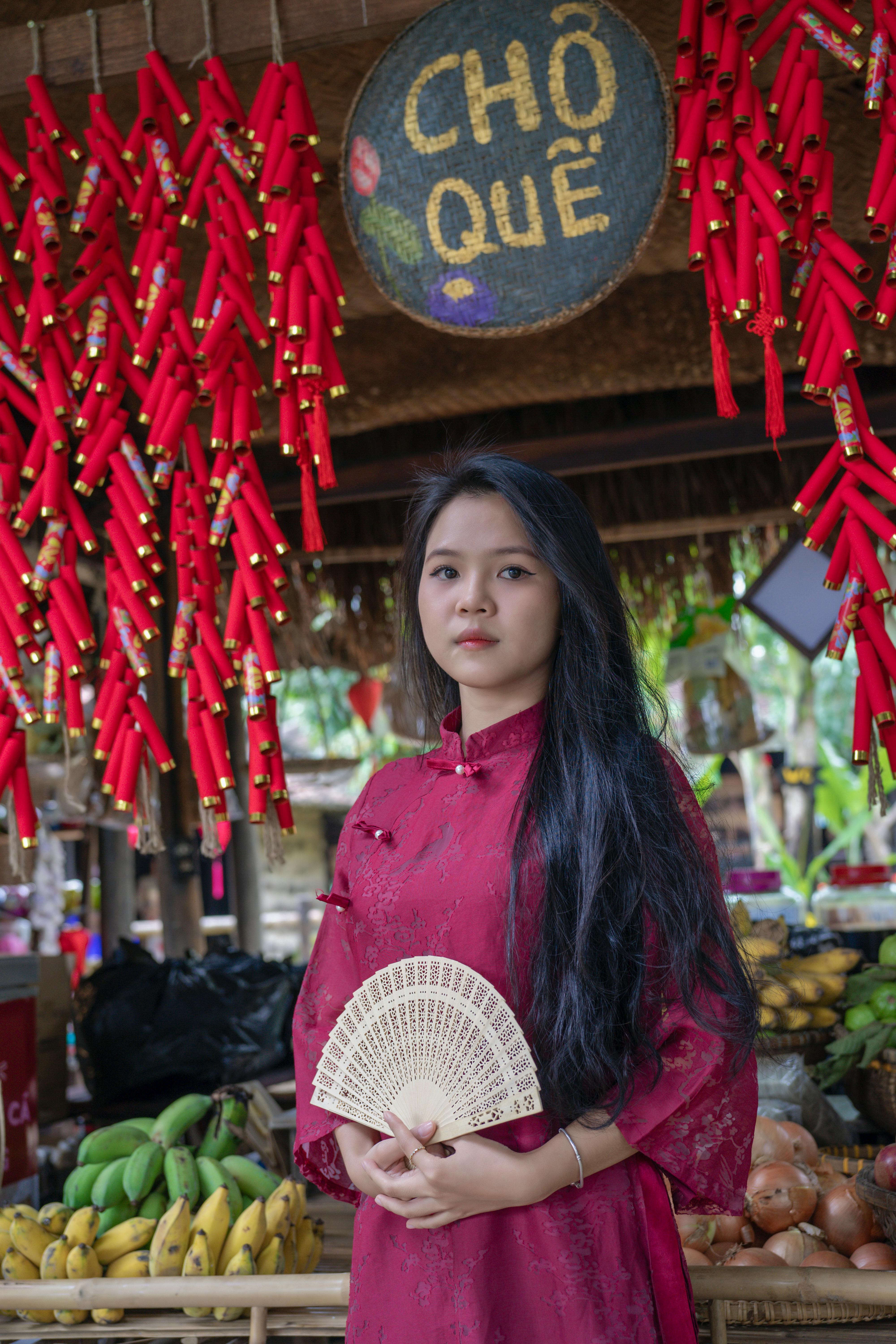 Portrait of a woman in traditional dress at a Vietnamese market stall.
