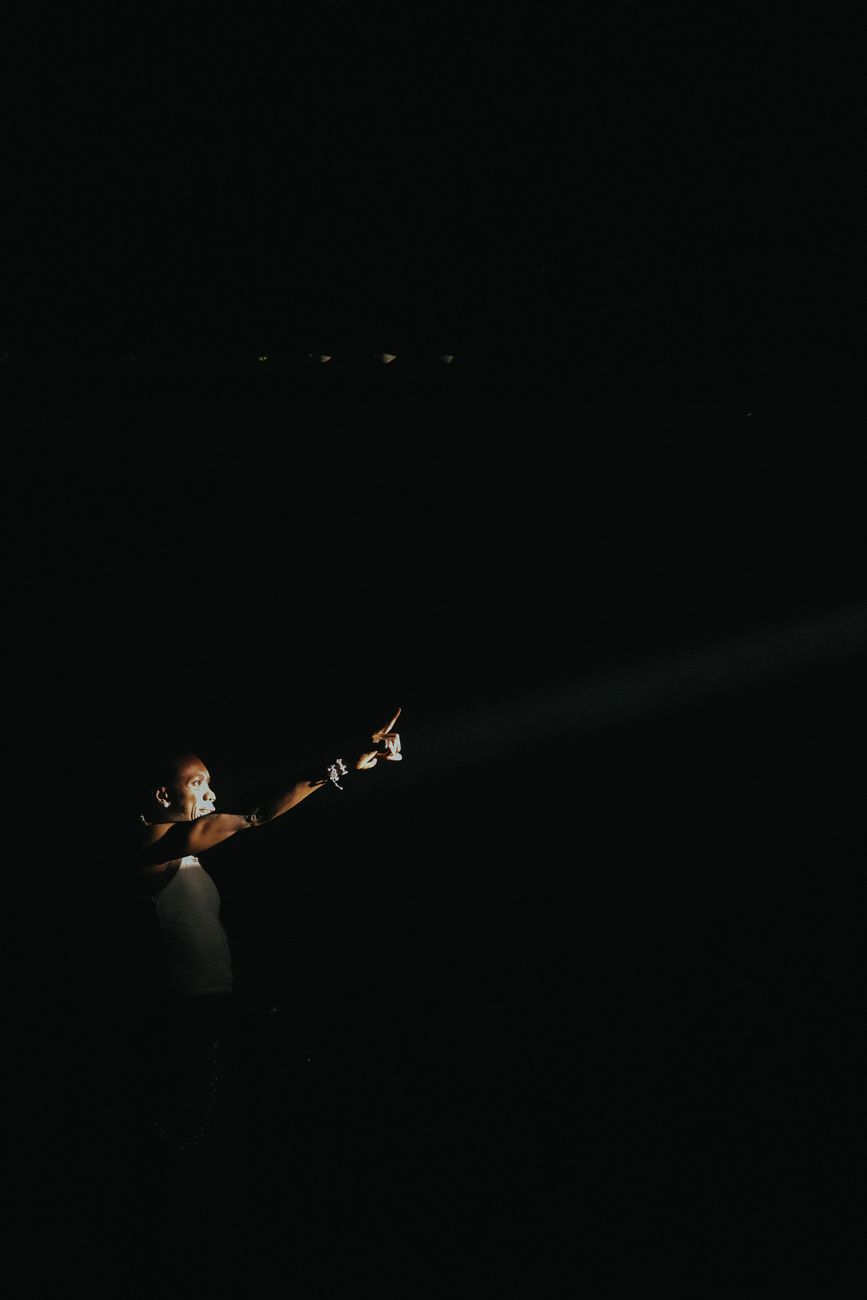Dramatisch beeld van een artiest op het podium onder een gerichte spot in een donkere ambiance.