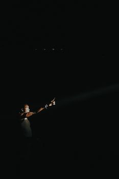 Dramatic image of a performer on stage under a focused spotlight in a dark ambiance.