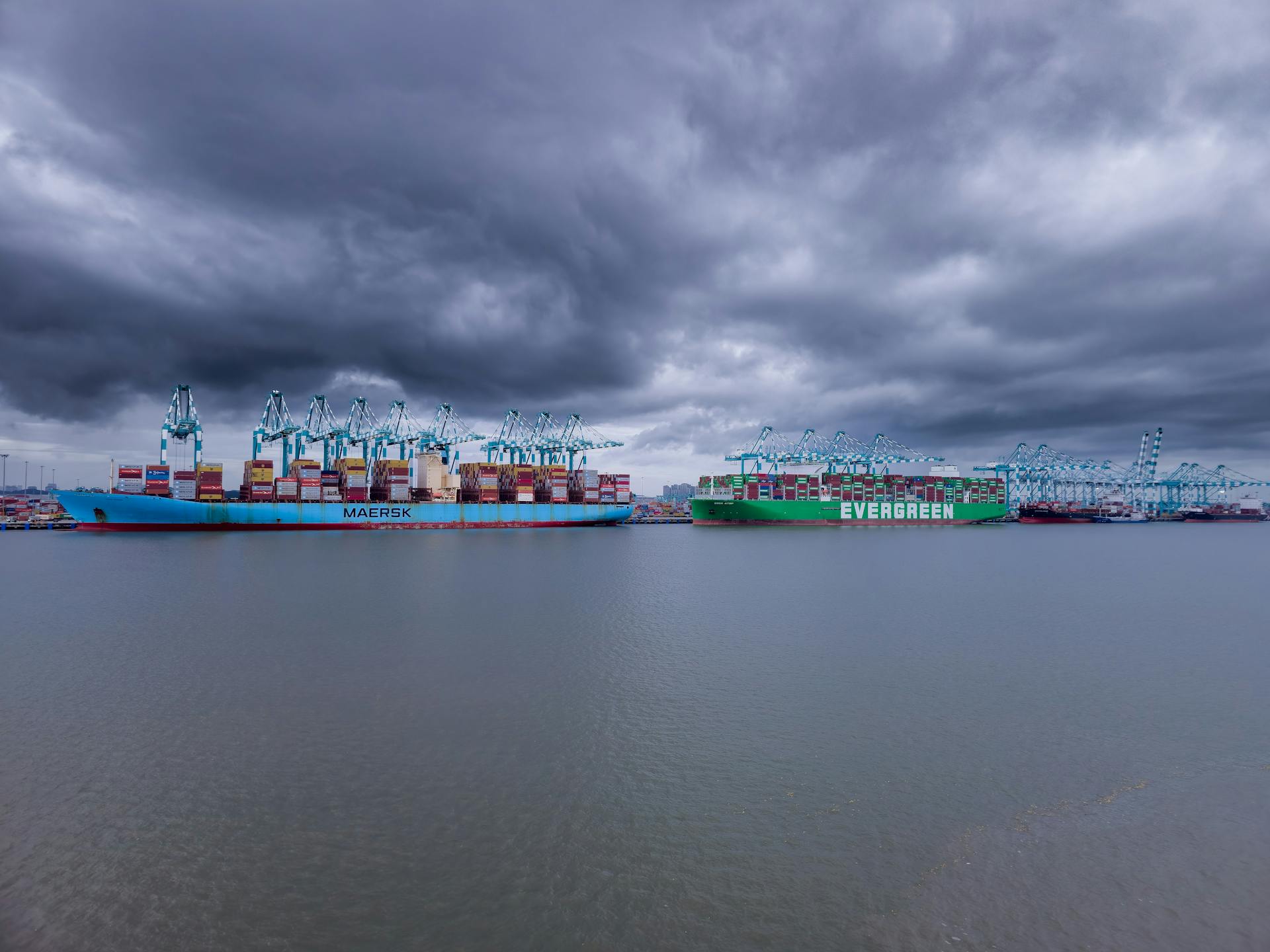Container ships in a harbor under dramatic storm clouds.