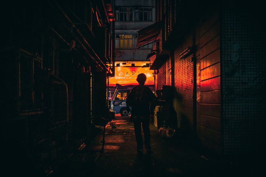 Silhouette of a person walking in a dimly lit alleyway with warm neon illumination