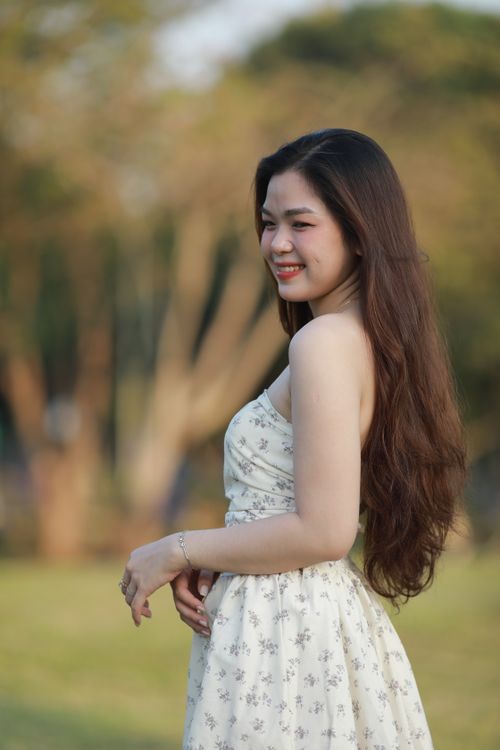 Free Happy woman in a white floral dress, enjoying a sunny day outside. Stock Photo