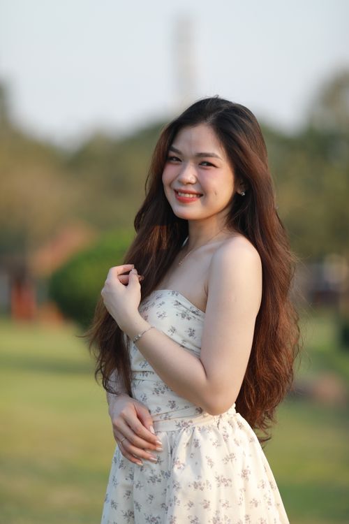 Free Portrait of a young woman in a white dress smiling under the sun outdoors. Stock Photo