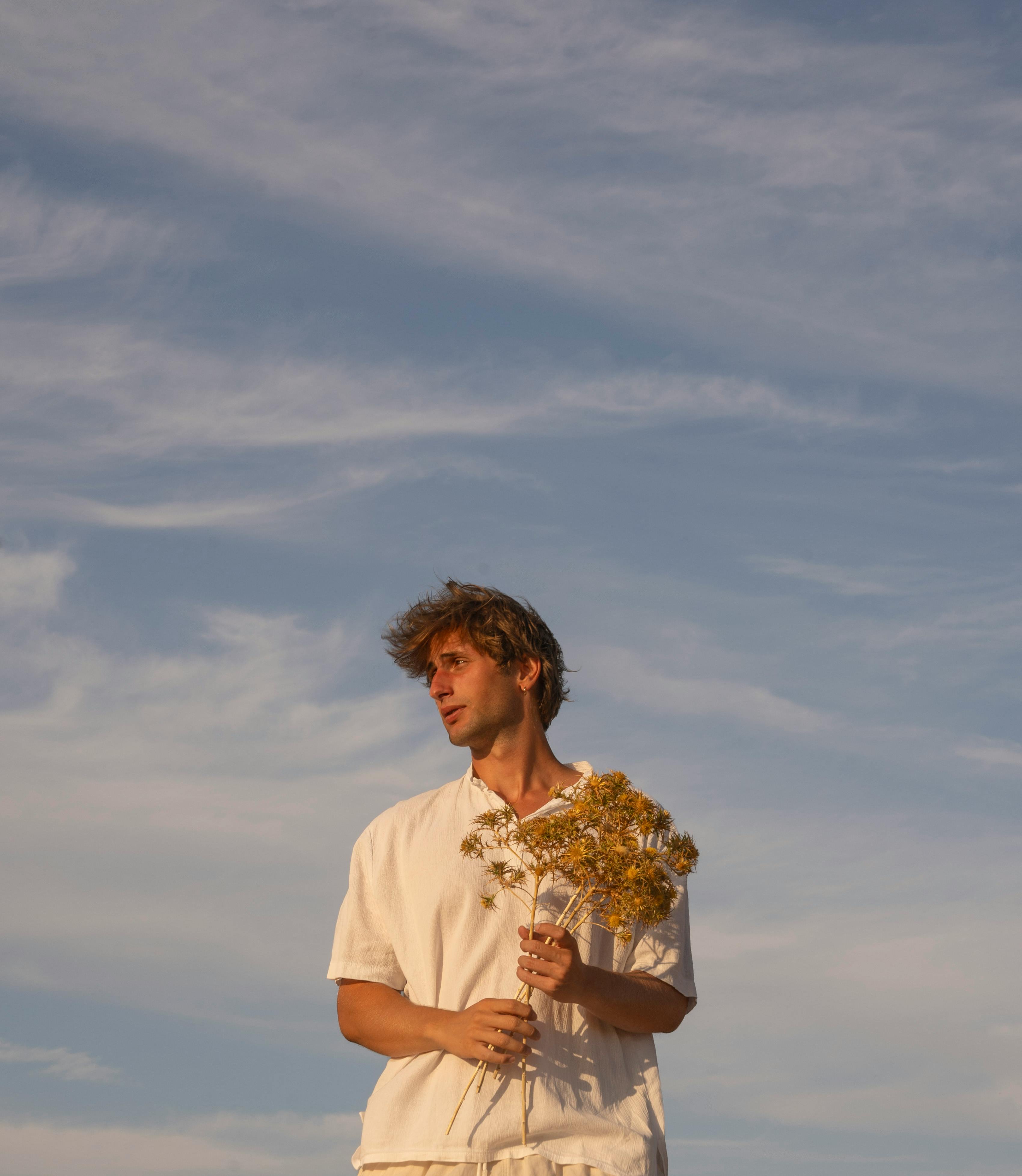 Outdoor portrait of a man holding flowers under a blue sky, exuding calmness.