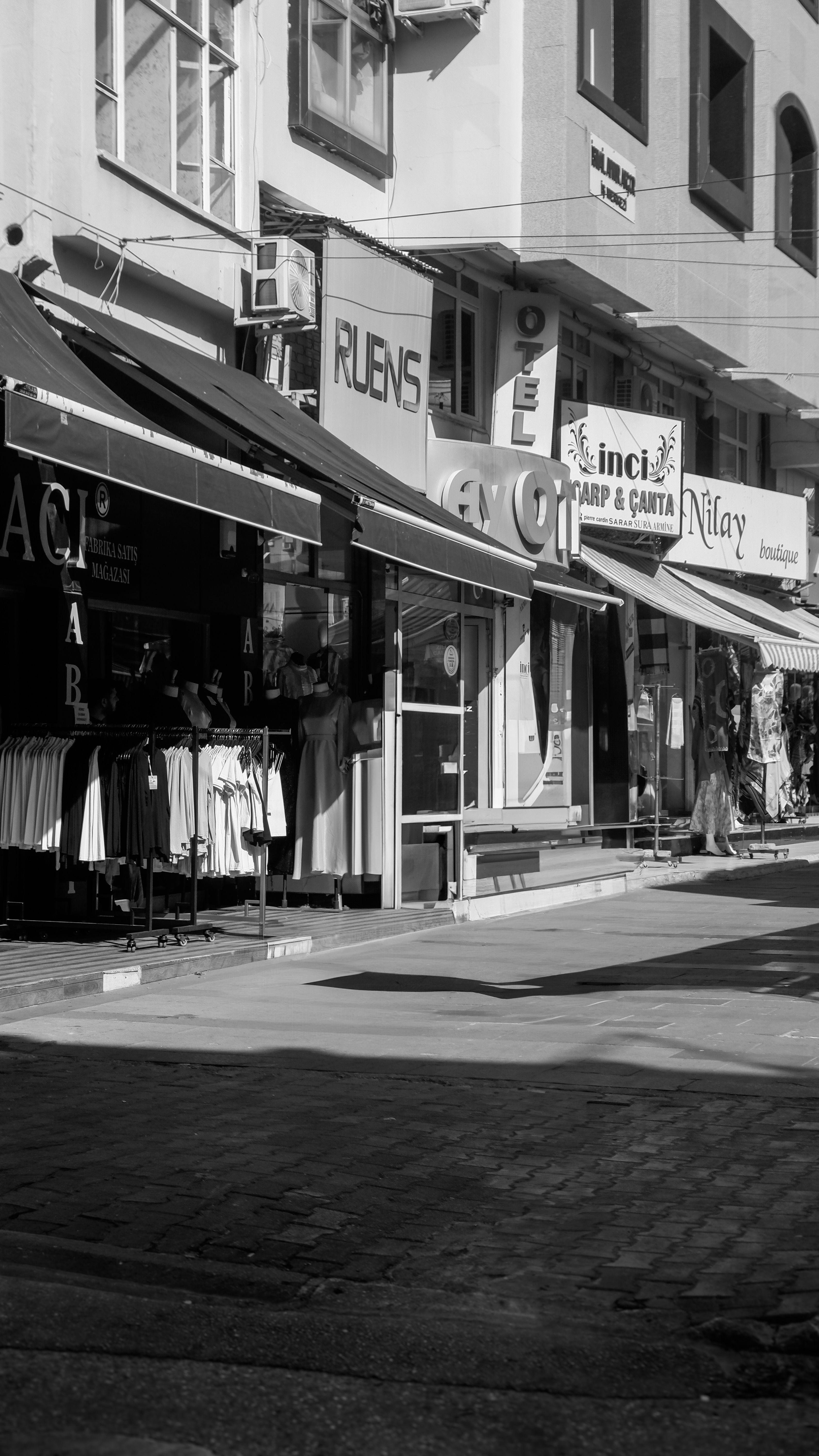 Monochrome urban street scene with clothing shops and signs.