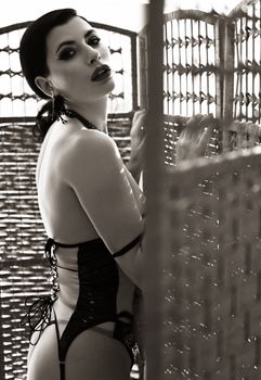 Sophisticated woman posing in vintage lingerie behind wicker screen in sepia tone.