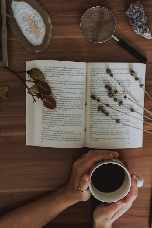 Mani Che Tengono Una Tazza Di Caffè E Un Libro Aperto Davanti