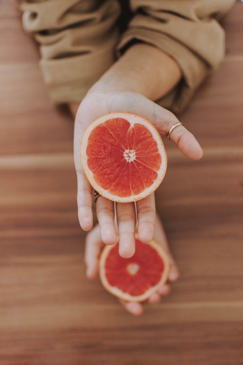 Free Close-up of hands presenting fresh grapefruit halves on wooden background. Stock Photo