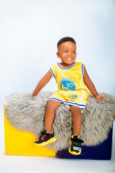 Happy young boy in basketball jersey sitting on a colorful stool, smiling confidently.