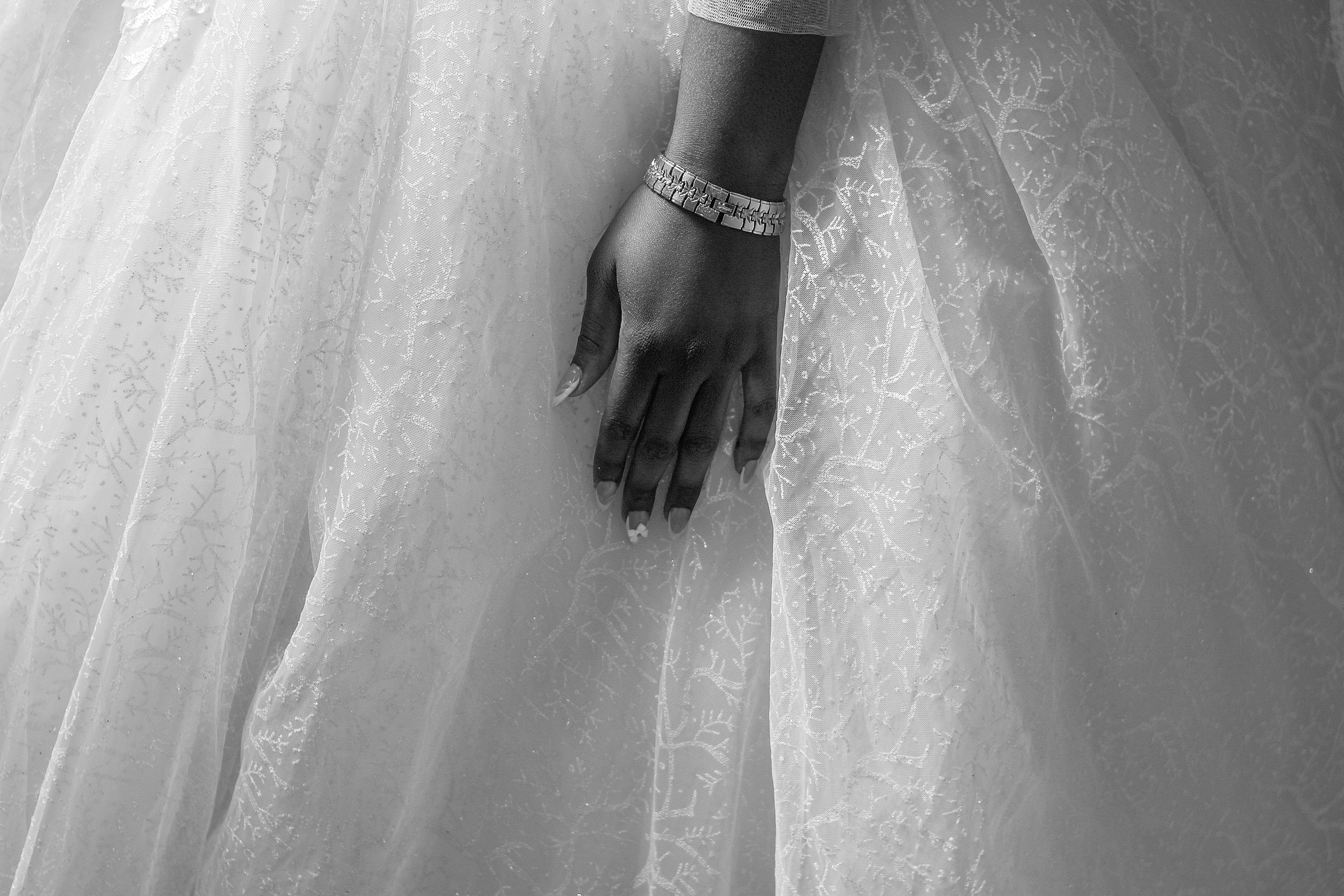 Black and white close-up of a bride's hand gracefully resting on her wedding dress, exuding elegance.