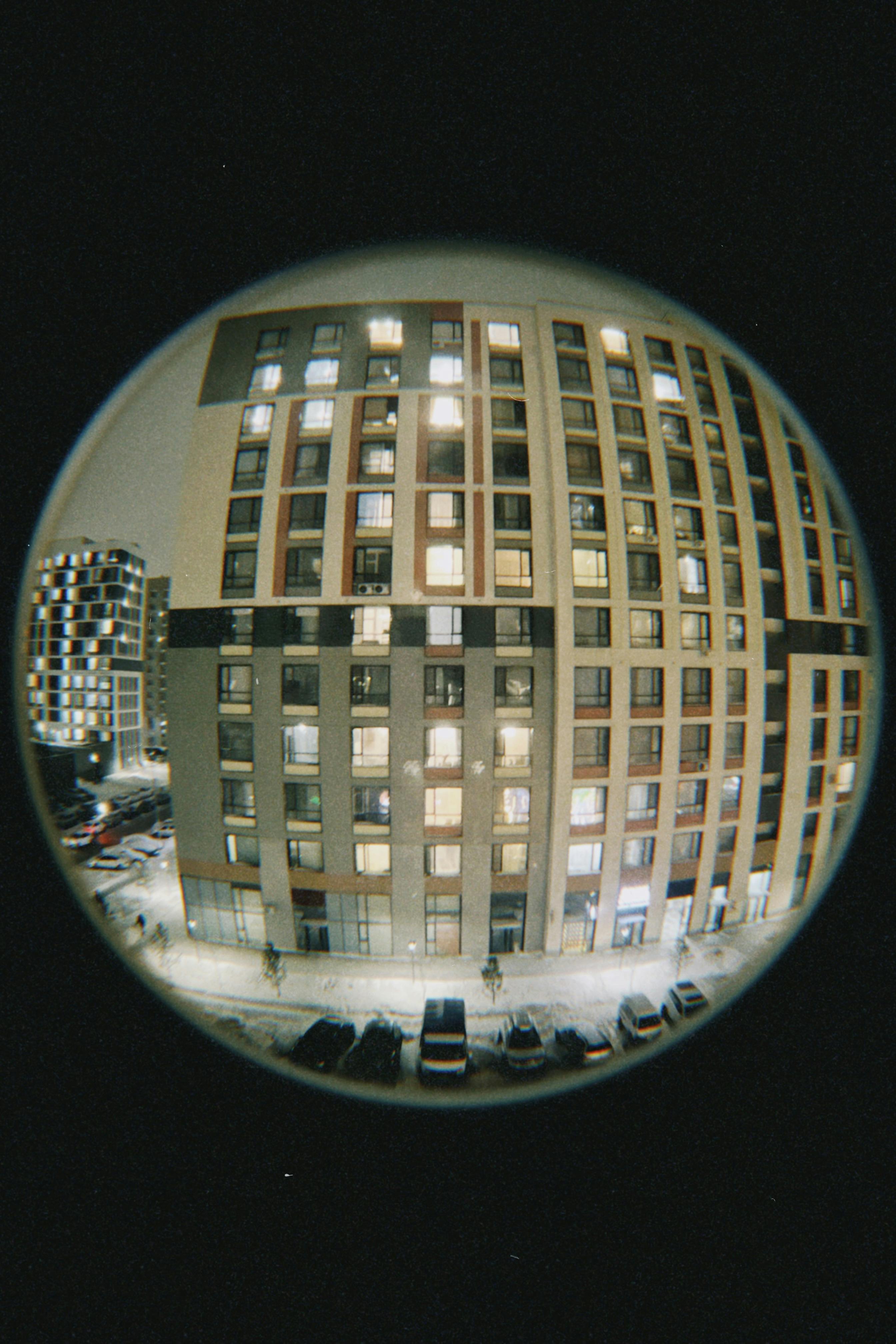 A fisheye lens captures urban apartment buildings illuminated at night.