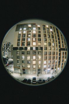A fisheye lens captures urban apartment buildings illuminated at night.